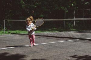 girl holding lawn tennis racket while standing beside white and black net